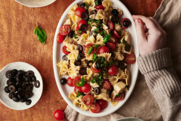 caprese pasta salad recipe plate with the ingredients on a table and one hand