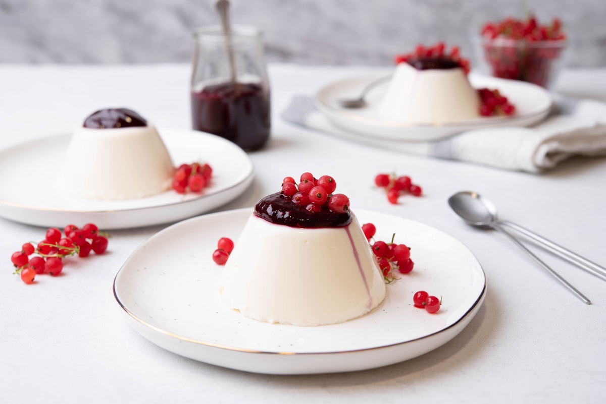 panna cotta on a plate topped with berries sauce and fresh berries