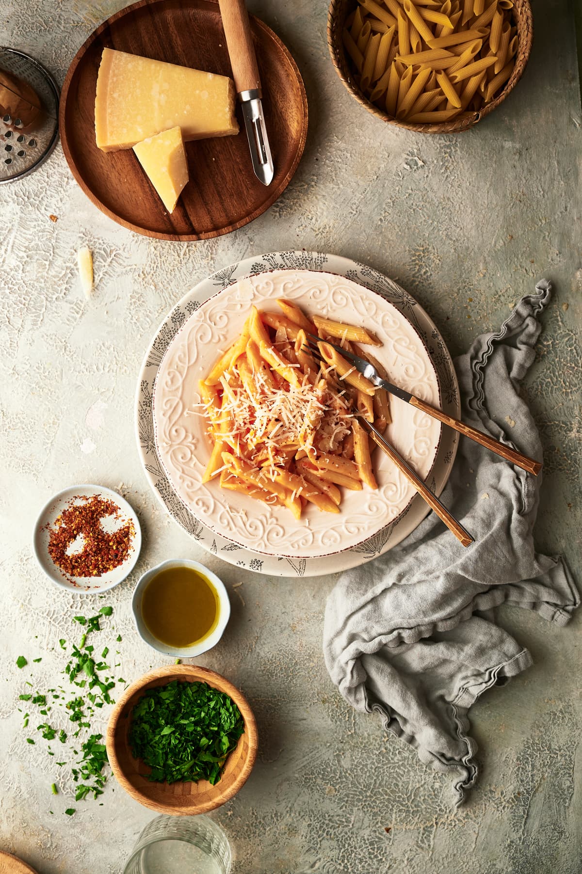 image of a dish with pasta with vodka sauce on a table next to dry pasta, parmigiano, parsley and red pepper flakes