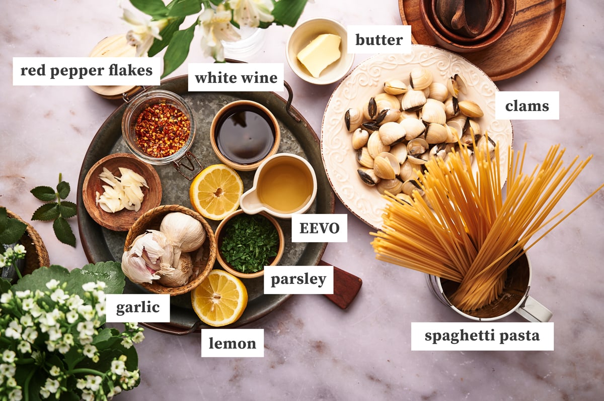 ingredients for spaghetti alle vongole recipe on a table: red pepper flakes, white wine, butter, clams, spaghetti pasta, parsley, extra virgin olive oil,  garlic and lemon