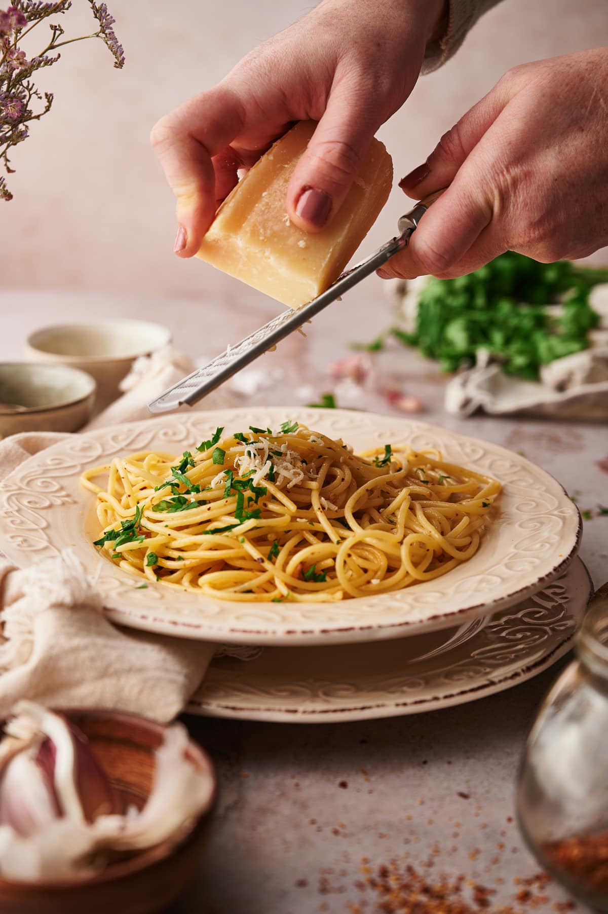 picture of a plate with spaghetti aglio e olio and two hands that grate parmigiano reggiano on top of it.
