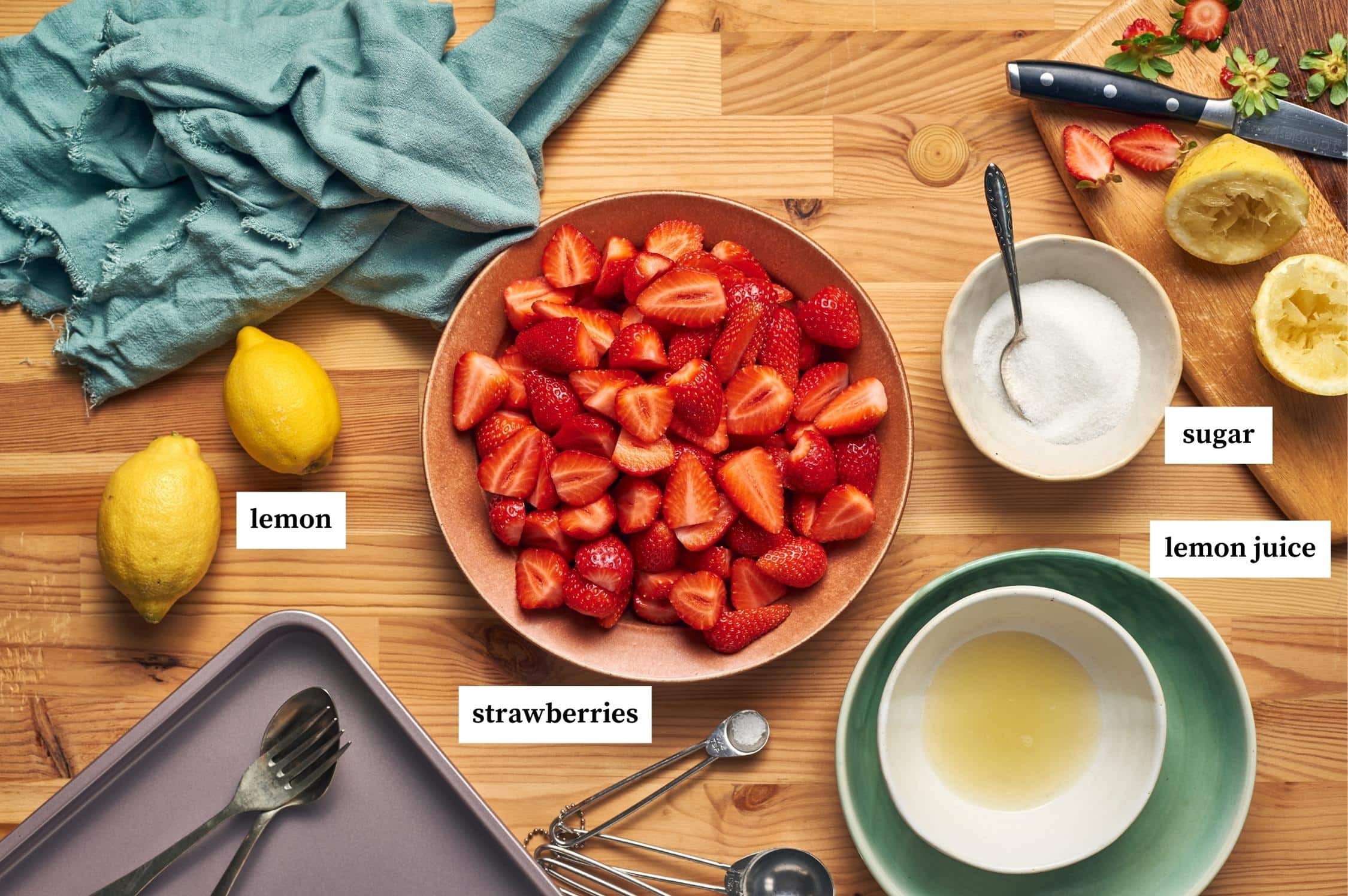 strawberry granita ingredients on a table: strawberries, lemon, sugar, lemon juice or water.