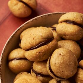 a bowl of baci di dama on top of a red brick table.