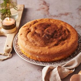 italian sponge cake on a plate, on top of a marble counter top with a wooden chopping board with candles and vase of flowers