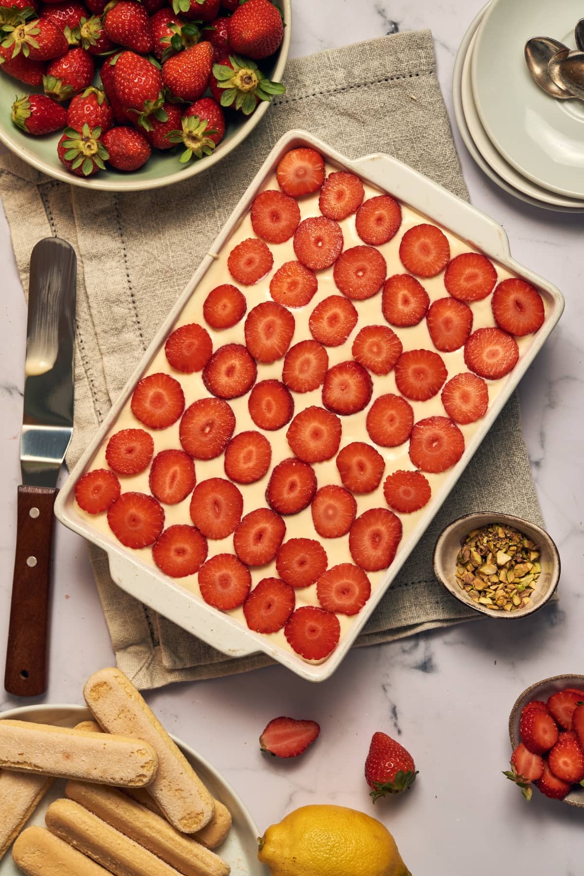 final strawberry tiramisu in a baking dish on a table next to ingredients