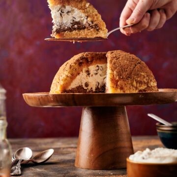 wooden cake stand with a zuccotto. a hand holding a cake cutter and a slice of zuccotto