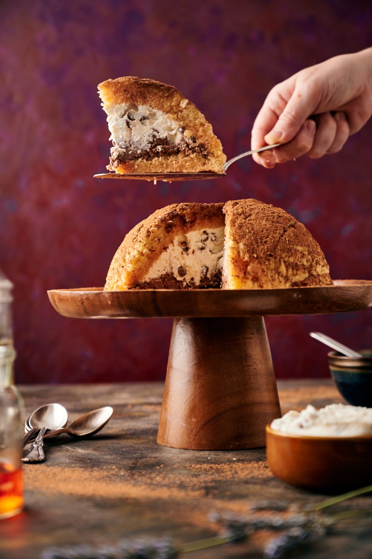 wooden cake stand with a zuccotto. a hand holding a cake cutter and a slice of zuccotto