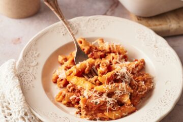 a dish of baked penne in a white plate next to a rectangular baking dish of baked penne.