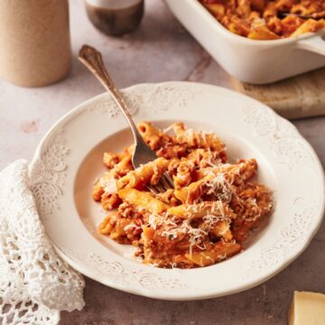 a dish of baked penne in a white plate next to a rectangular baking dish of baked penne.