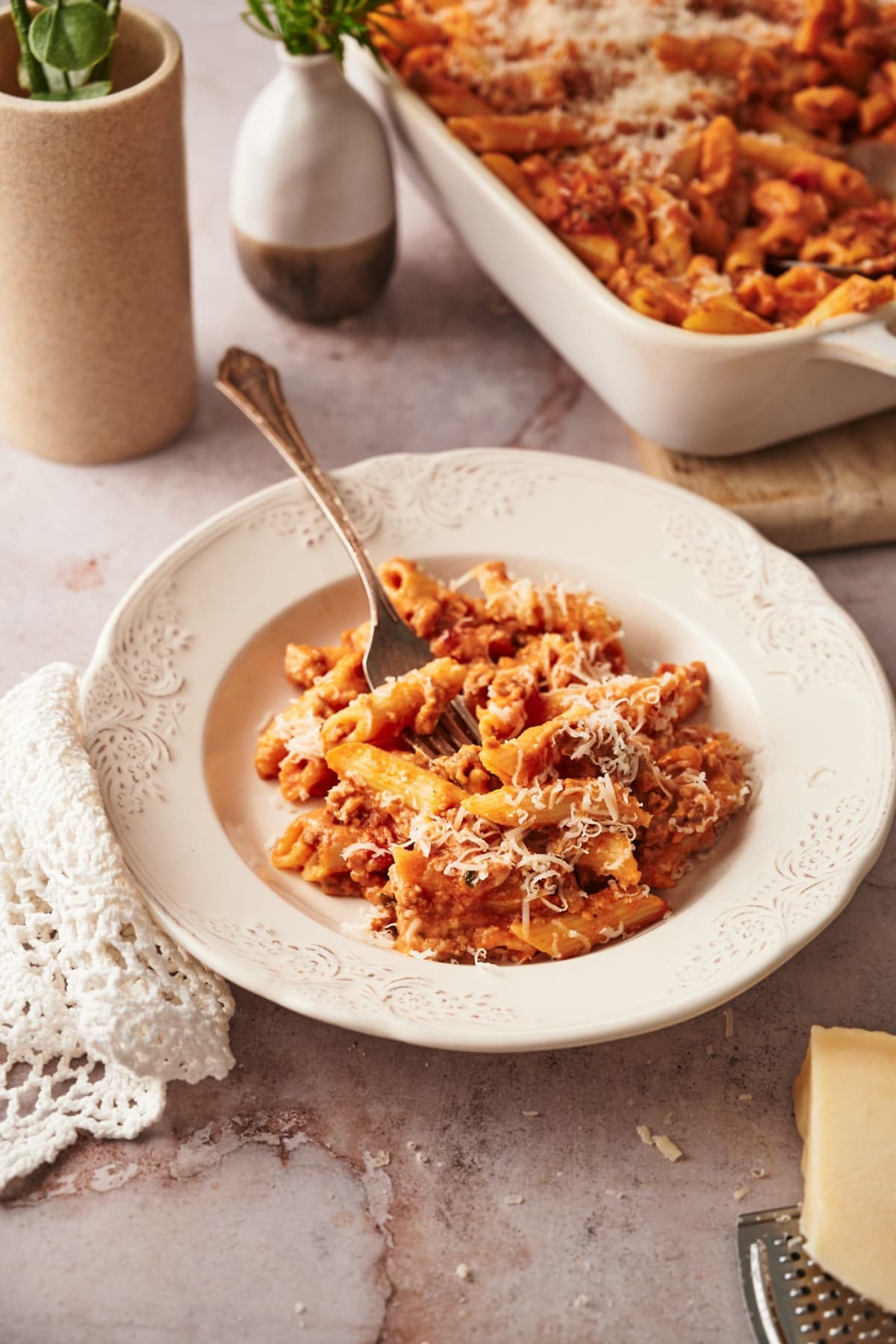 a dish of baked penne in a white plate next to a rectangular baking dish of baked penne.