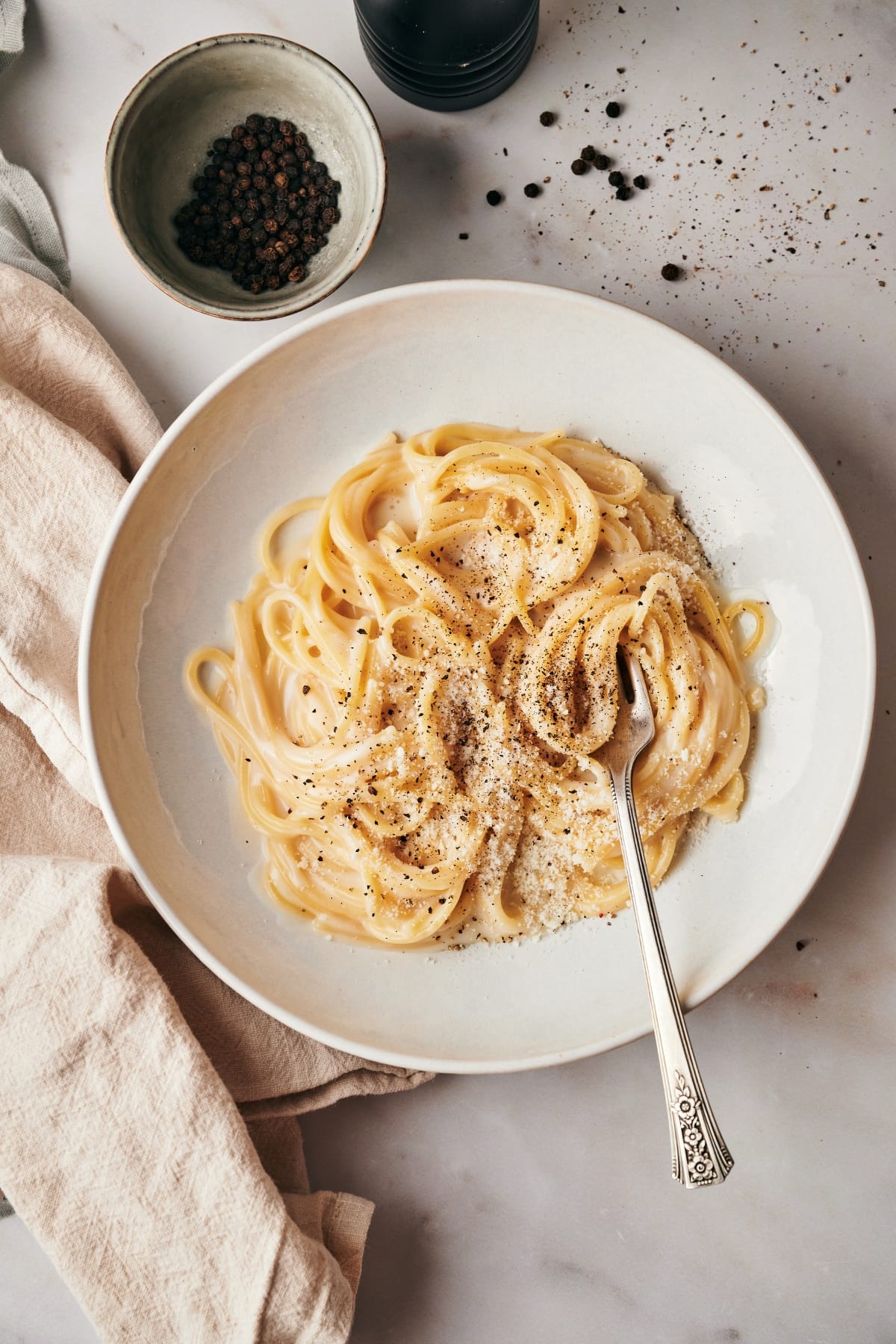 finished cacio e pepe on a white plate with a silver fork and a table napkin underneath the plate