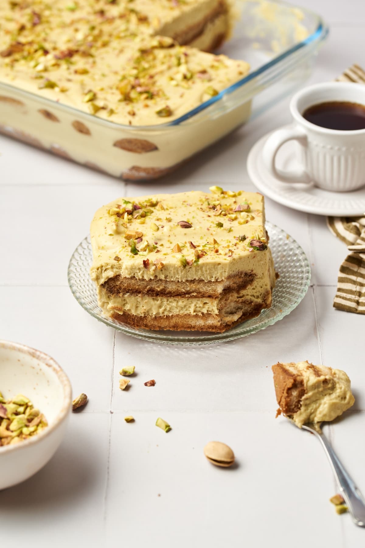 Pistachio tiramisu on a crystal plate beside a cup of coffee